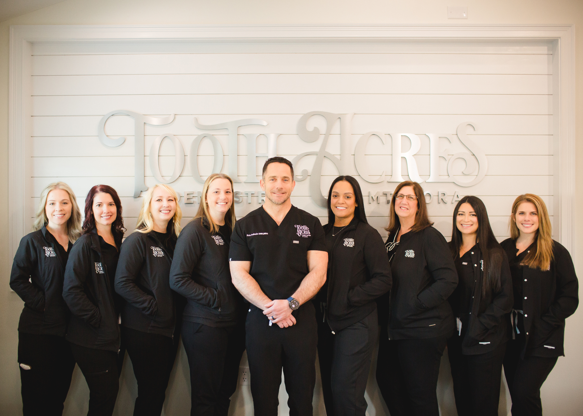 The Tooth Acres Dentistry team — Dr. Rob Pellosie with hygienists, assistants, and front-desk staff in front of the Tooth Acres sign in Mount Dora, FL