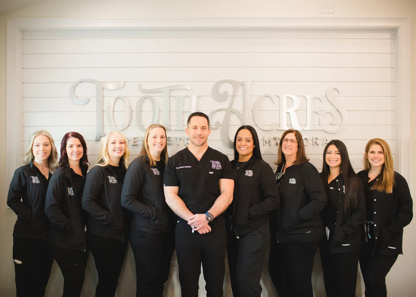 The Tooth Acres Dentistry team — Dr. Pellosie with hygienists, assistants, and front-desk staff in front of the Tooth Acres sign in Mount Dora, FL